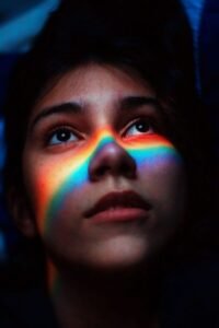 Portrait of a woman with a rainbow light across her face, capturing a moody and artistic feel.