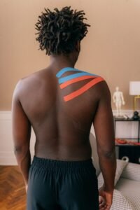 Back view of a male athlete with kinesiology tapes applied to the shoulder indoors.