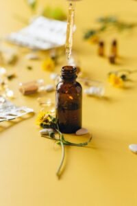 Brown glass bottle with dropper and yellow flowers on a yellow surface.